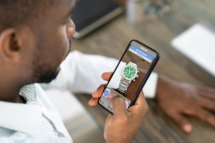 A man uses a smartphone to virtually try a watch on his wrist.