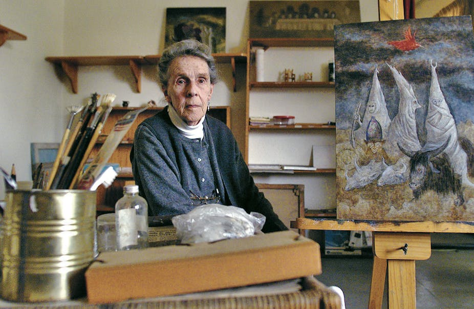 An elderly Carrington sat in her studio, with a painting behind her and brushes to her side. 