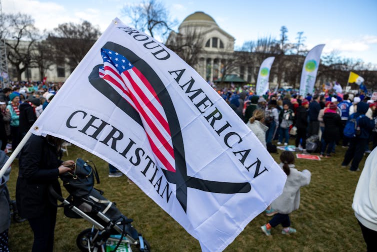 Una bandera blanca con un símbolo religioso y la bandera estadounidense combinada con las palabras 