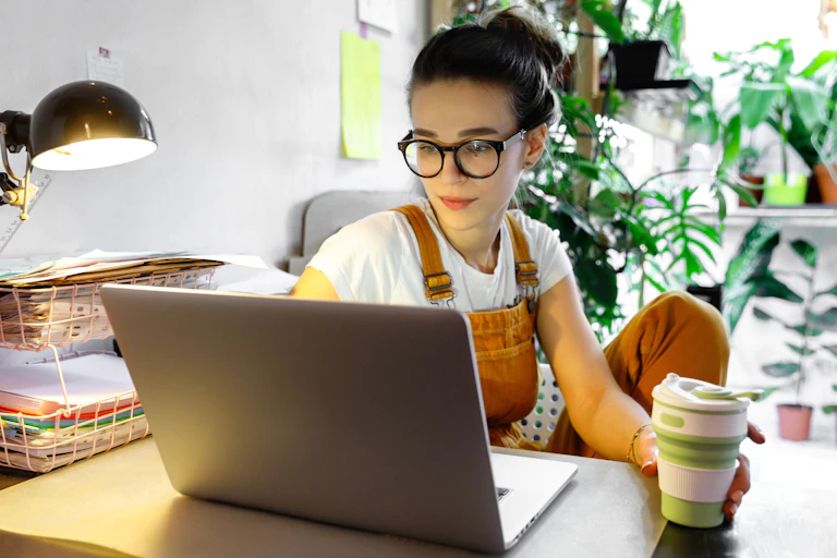 Woman works at a desk with papers, a coffee and laptop.