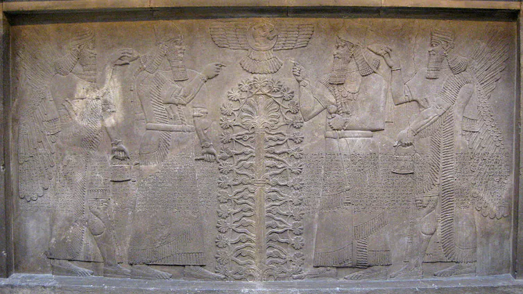 A worn stone carving of winged figures on either side of a tree.