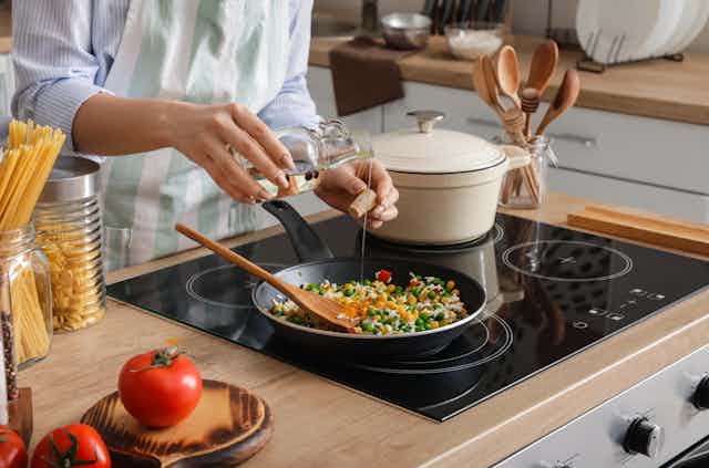 Woman cooking tasty rice with vegetables on induction (electric) stovetop in kitchen, closeup