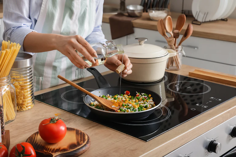 Woman cooking tasty rice with vegetables on induction (electric) stovetop in kitchen, closeup