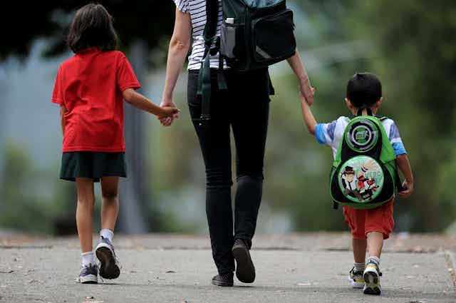 A parent walks two young children to school.
