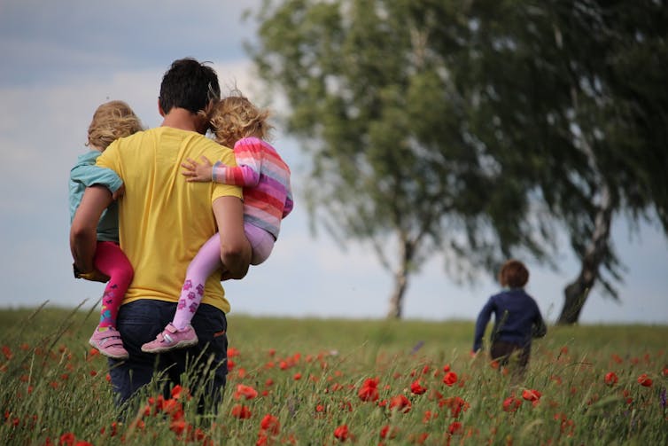 Dad carries his twins in a field, while an older child runs ahead