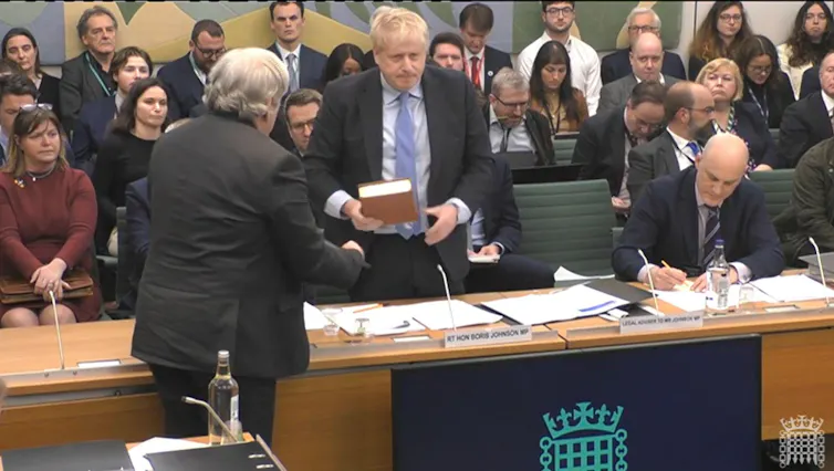 Boris Johnson swearing on a bible in a parliament committee room.
