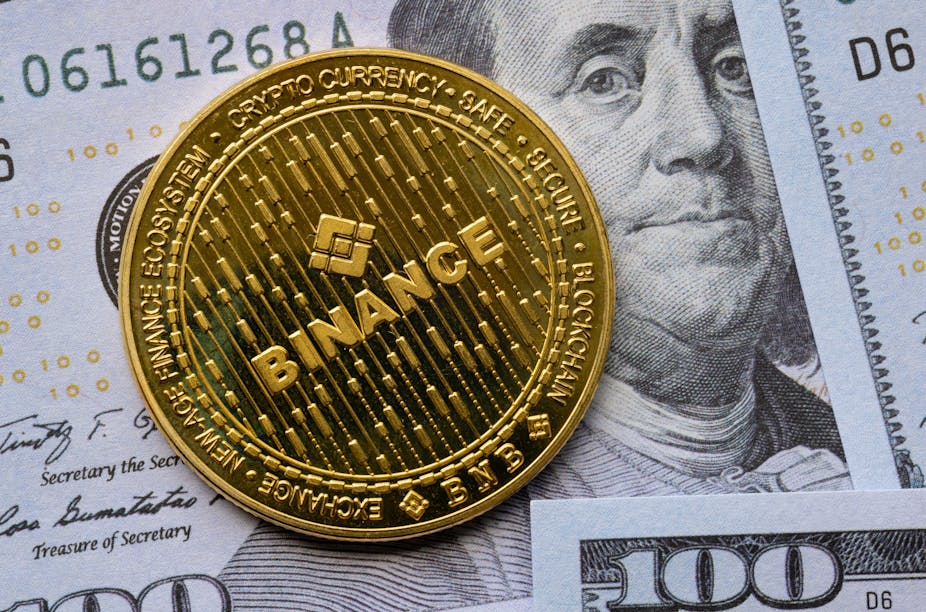 Binance "coin" on top of a US$100 bill showing Ben Franlin's face.