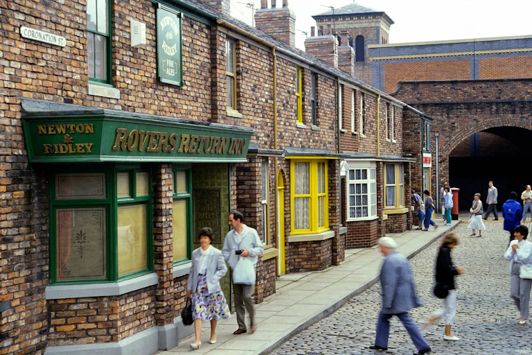 A TV set featuring a street with a railway arch and shops with pedestrians.