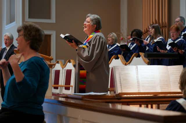 A pastor sings while standing in front of a choir.