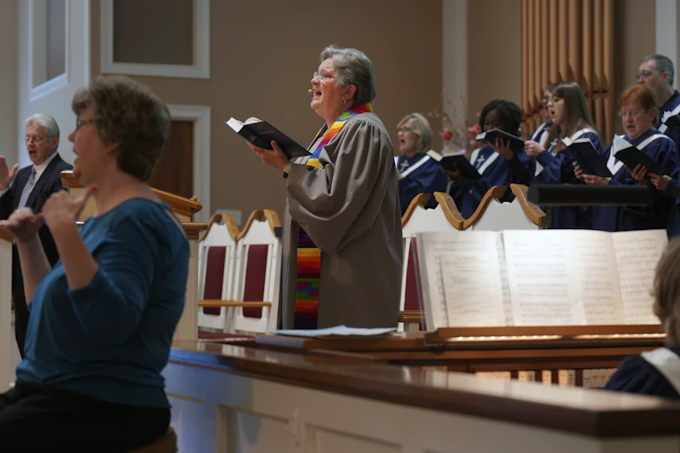 A pastor sings while standing in front of a choir.