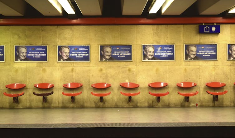 A subway station with multiple posters featuring the face of a smiling man over a row of empty seats.