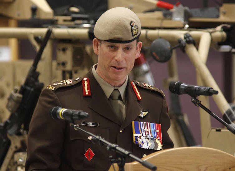 A man in a beige beret and military uniform speaks into a microphone.