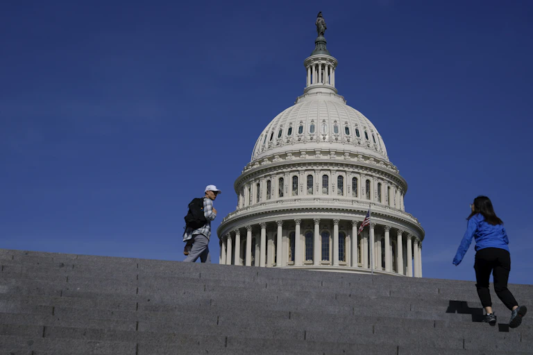A young woman seen from the back climbing a wide set of granite steps with a large, ornate domed building in the background
