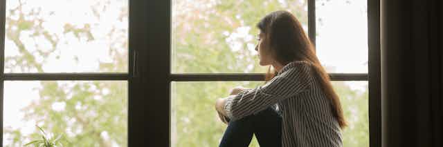 An unhappy-looking woman stares out a window.