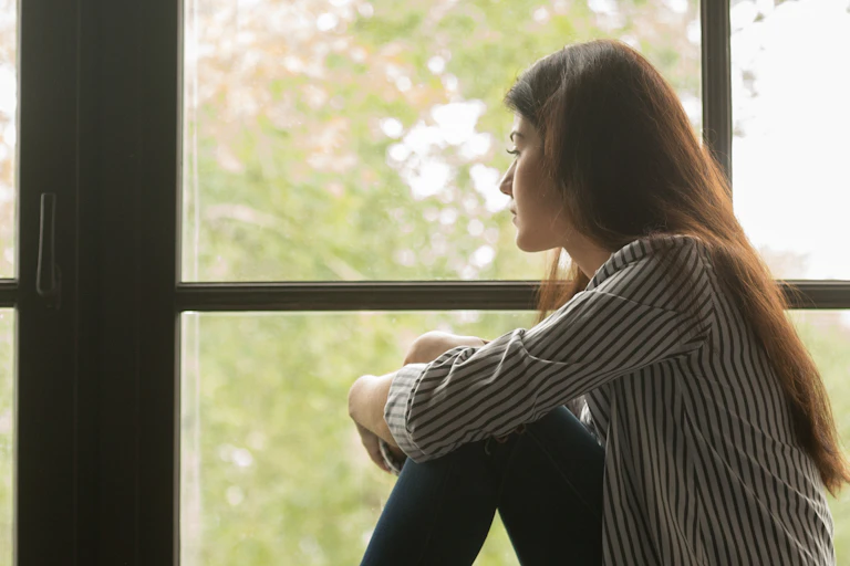 An unhappy-looking woman stares out a window.