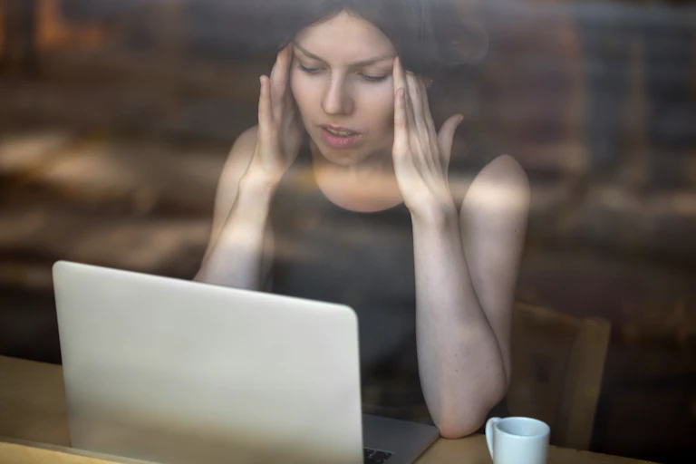 Une jeune femme se prend la tête alors qu'elle regarde son écran d'ordinateur