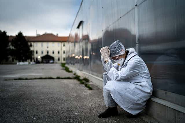 Femme en blouse et masque anti-Covid épuisée assise à l'extérieur d'un bâtiment