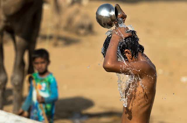 Child pours water over himself from a metal container.
