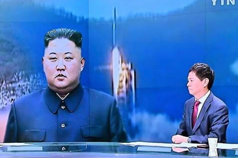 Male newsreader in suit at desk, in front of images of Kim Jong-un and a launching rocket