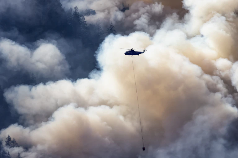 Wildfire Service helicopter flying over British Columbia forest fire.