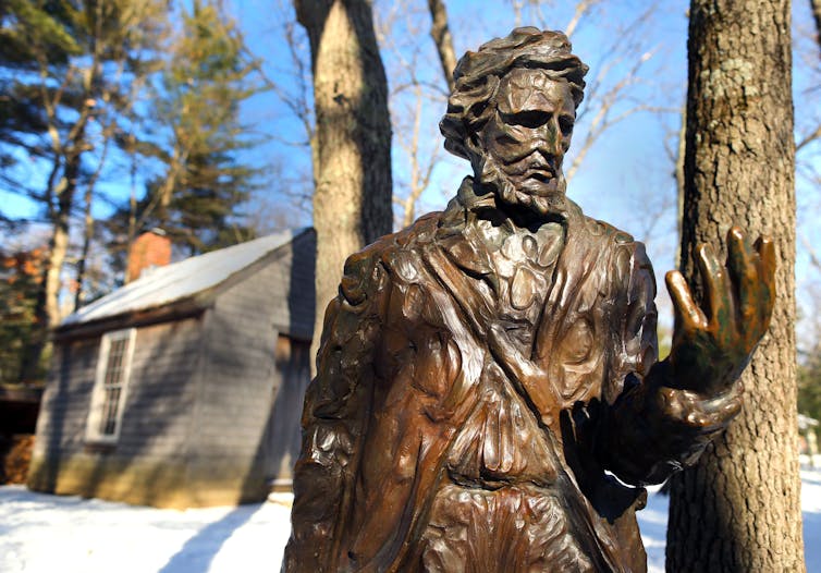 A statue of Henry David Thoreau in front of a reproduction of his cabin at the Walden Pond Reservation in Concord, Massachusetts.