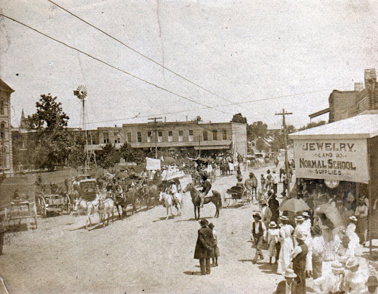 In this black and white image, Black men and women are seen marching along a main street while others are watching.