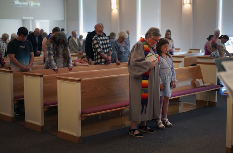 A female pastor leads the prayer in a church as the congregation stands behind her.