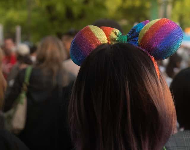 A woman with a rainbow colored mouse ears on her head.