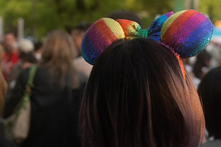 A woman with a rainbow colored mouse ears on her head.