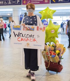 A woman wearing a face mask carrying a sign that reads: Welcome to Canada.