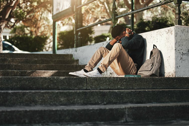 A young man sitting on stairs outdoors, appears upset.