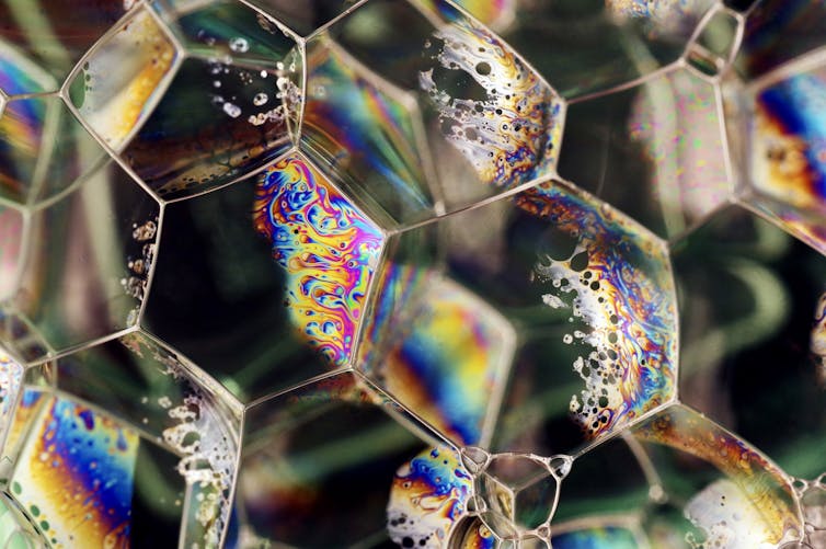 A tightly packed collection of hexagon-shaped, rainbow-colored bubbles against a dark background