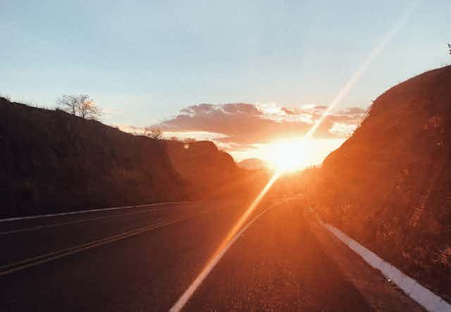 A low angle shot of an asphalt road with the sun shining low on the horizon