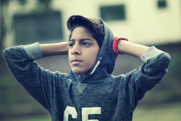 A young boy puts his hands on his head.