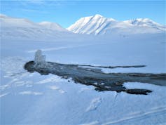 A small fountain of water in an opening in the ice, amid a snowy landscape.