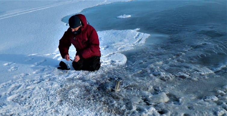 Scientist crouched on ice taking water samples.
