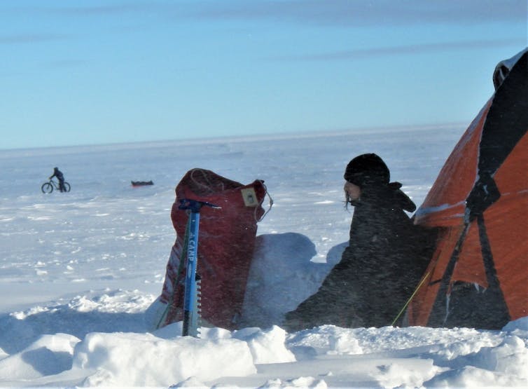 Scientist sitting outside her tent with backpack, looking out at icy landscape.