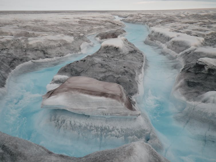 A landscape of dark ice intertwined with blue rivers of meltwater.