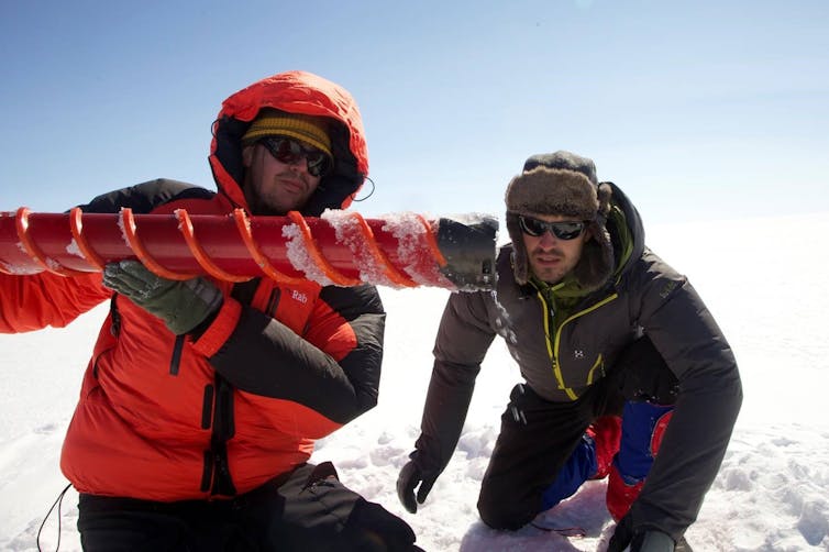 Two scientists inspecting an ice corer device dripping with meltwater.