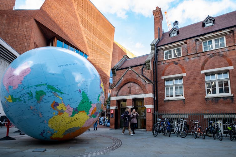 A sculpture of a globe in front of a brick building.