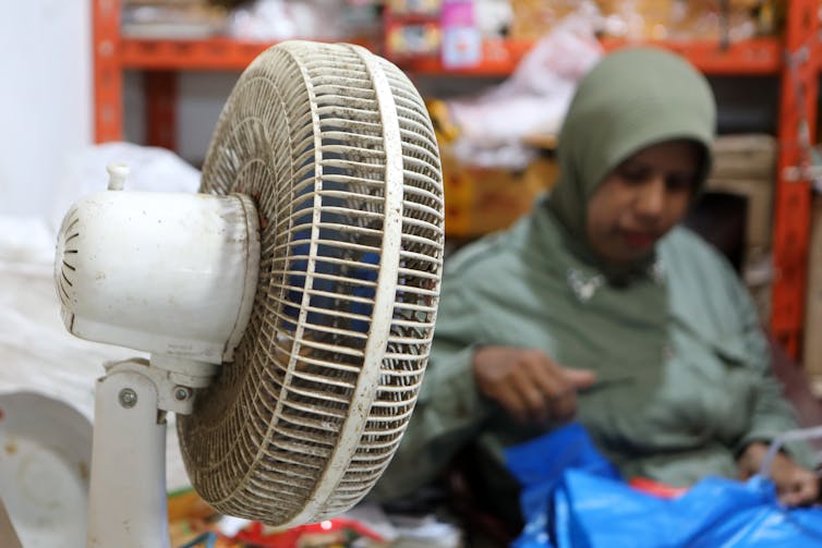 شخص يرتدي الحجاب يعمل في سوق بجوار مروحة كهربائية.