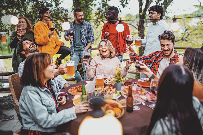 A group of adults laugh around a patio table while enjoying alcoholic drinks.