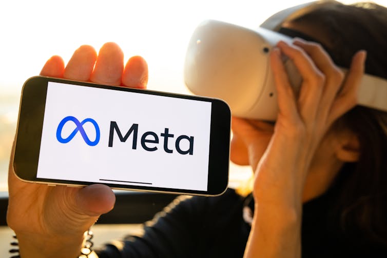 Woman holding smartphone with new facebook logo wearing Oculus VR headset