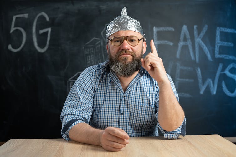 Close-up of a male conspiracy theorist in a protective foil cap and glasses debunks myths.