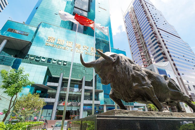 A statue of a bull outside a glass skyscraper with flags including China's flag.