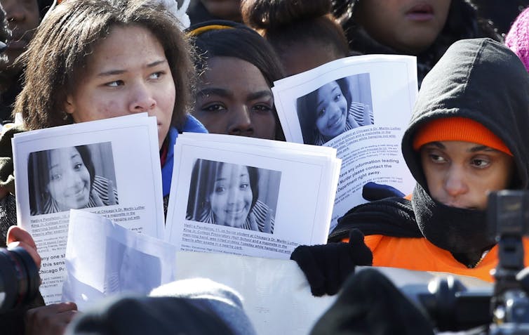 a group of people holding papers with a young girl's face printed on them
