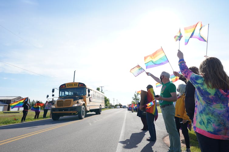 People seen standing holidng pride flags outside a school bus.
