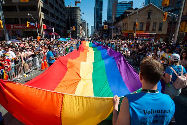 People at a pride parade carry a large rainbow flag.