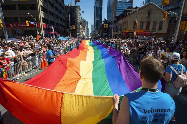 People at a pride parade carry a large rainbow flag.