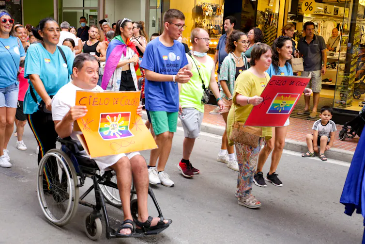A man in a wheelchair with people walking carrying placards.